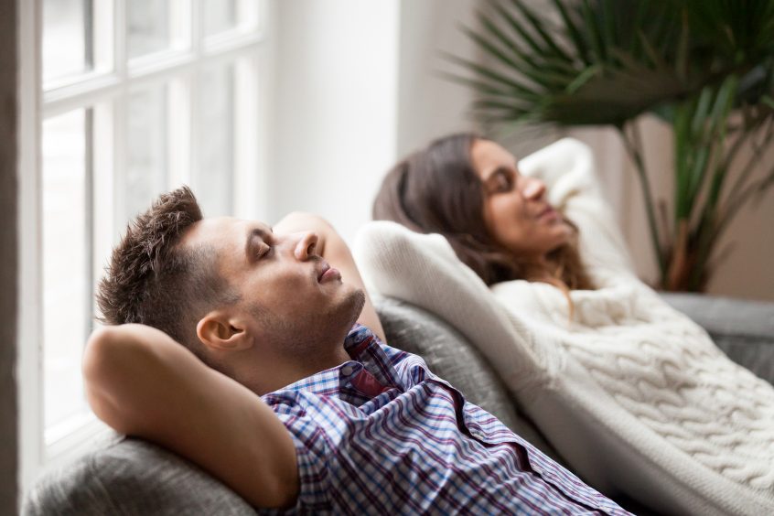 Young couple resting on comfortable couch together at home, happy man and woman enjoying relaxation or nap dozing on sofa with eyes closed, calm family breathing fresh air feeling totally relaxed